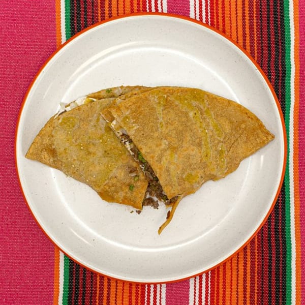 Two La Patrona quesadillas, one cut open to reveal meat and cheese, on a white plate.