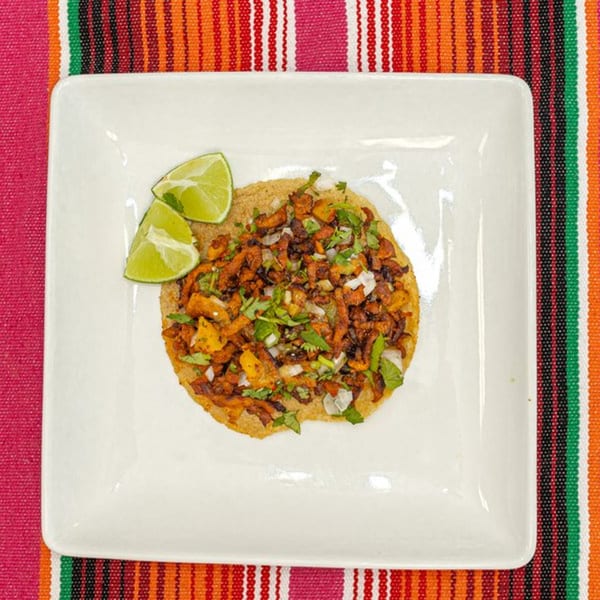La Patrona's Mexican tostada with seasoned meat, onions, cilantro, and lime wedges on a white plate.