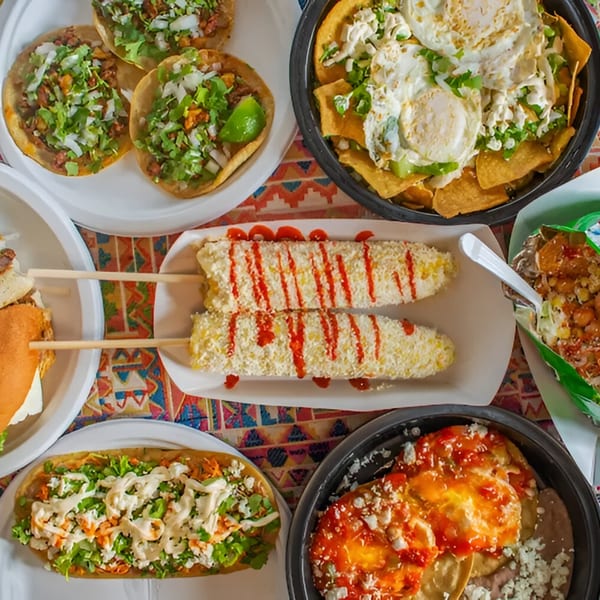 A vibrant spread of Mexican dishes, including tacos, elotes, nachos, and a torta.